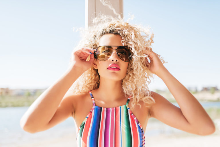 Woman with curly blonde hair in aviator sunglasses and a striped swimsuit